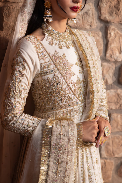 Naqshi Fasana dove‑white floor‑length raw‑silk frock with halter neckline, deep back, heavy hand‑adda—kora, dabka, sitari, tilla, crystal embellishments—and structured pouch.